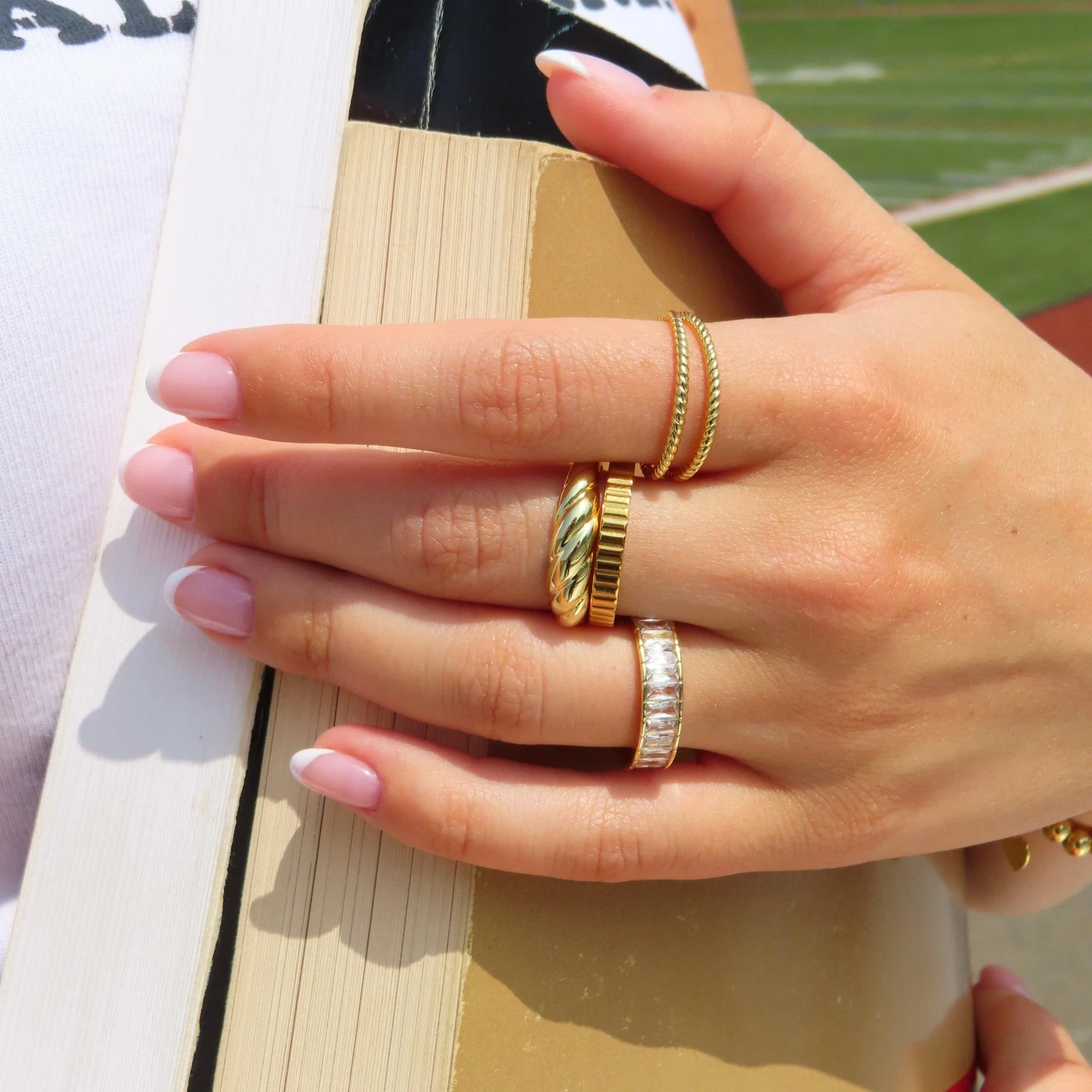 EVRY Jewels gold and silver rings worn on a hand holding a book